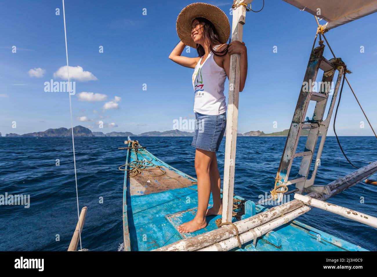 Philippinen, Palawan, El Nido, Bacuit-Archipel, junge philippinische Frau, die auf dem Bug eines Auslegerkanus auf dem Weg zur Miniloc-Insel steht Stockfoto