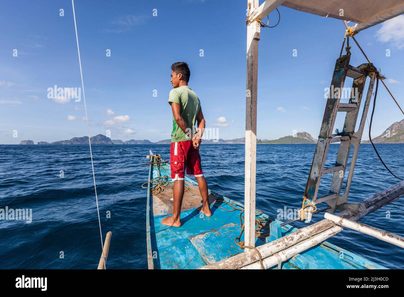 Philippinen, Palawan, El Nido, Bacuit-Archipel, junger philippinischer Seemann, der auf dem Bug seines Auslegerkanus auf dem Weg zur Insel Miniloc steht Stockfoto