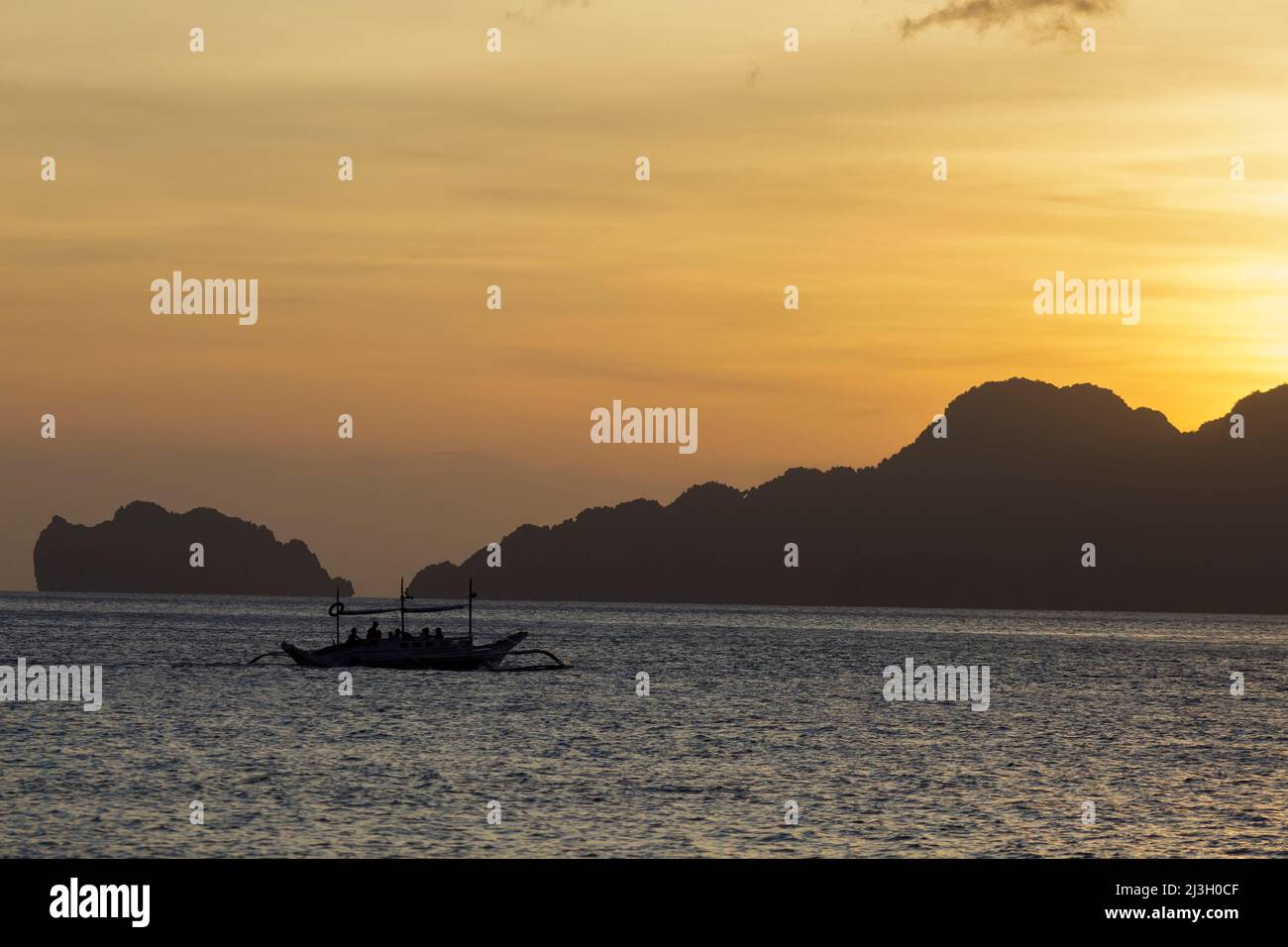 Philippinen, Palawan, El Nido, Bacuit-Archipel, Seven Commandos Beach, Hintergrundbeleuchtetes Auslegerkanu und Sonnenuntergang über kleinen felsigen Inseln Stockfoto
