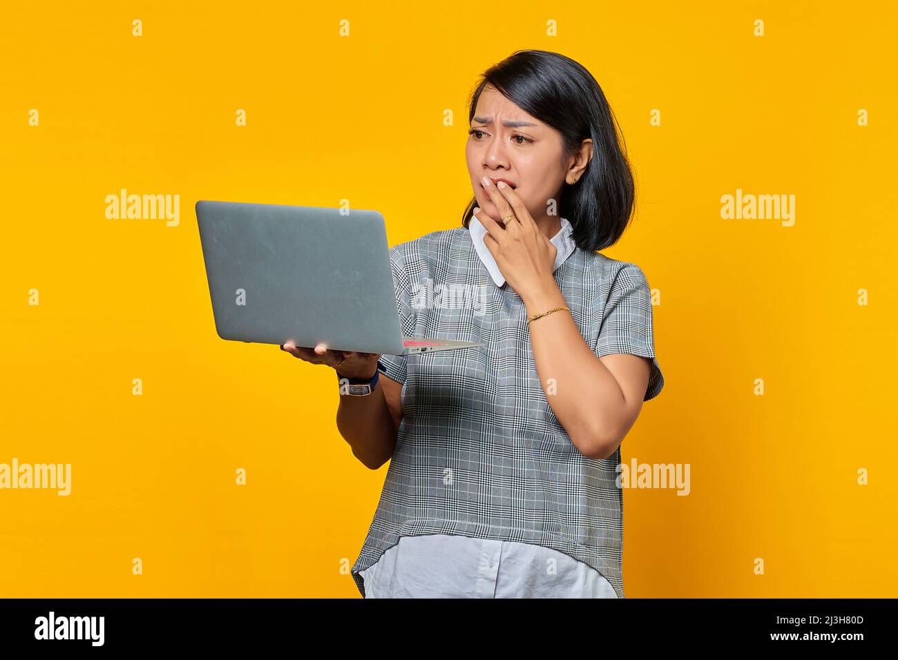 Schockiert asiatische Frau Blick auf Laptop mit Hand bedeckt Mund über gelben Hintergrund Stockfoto