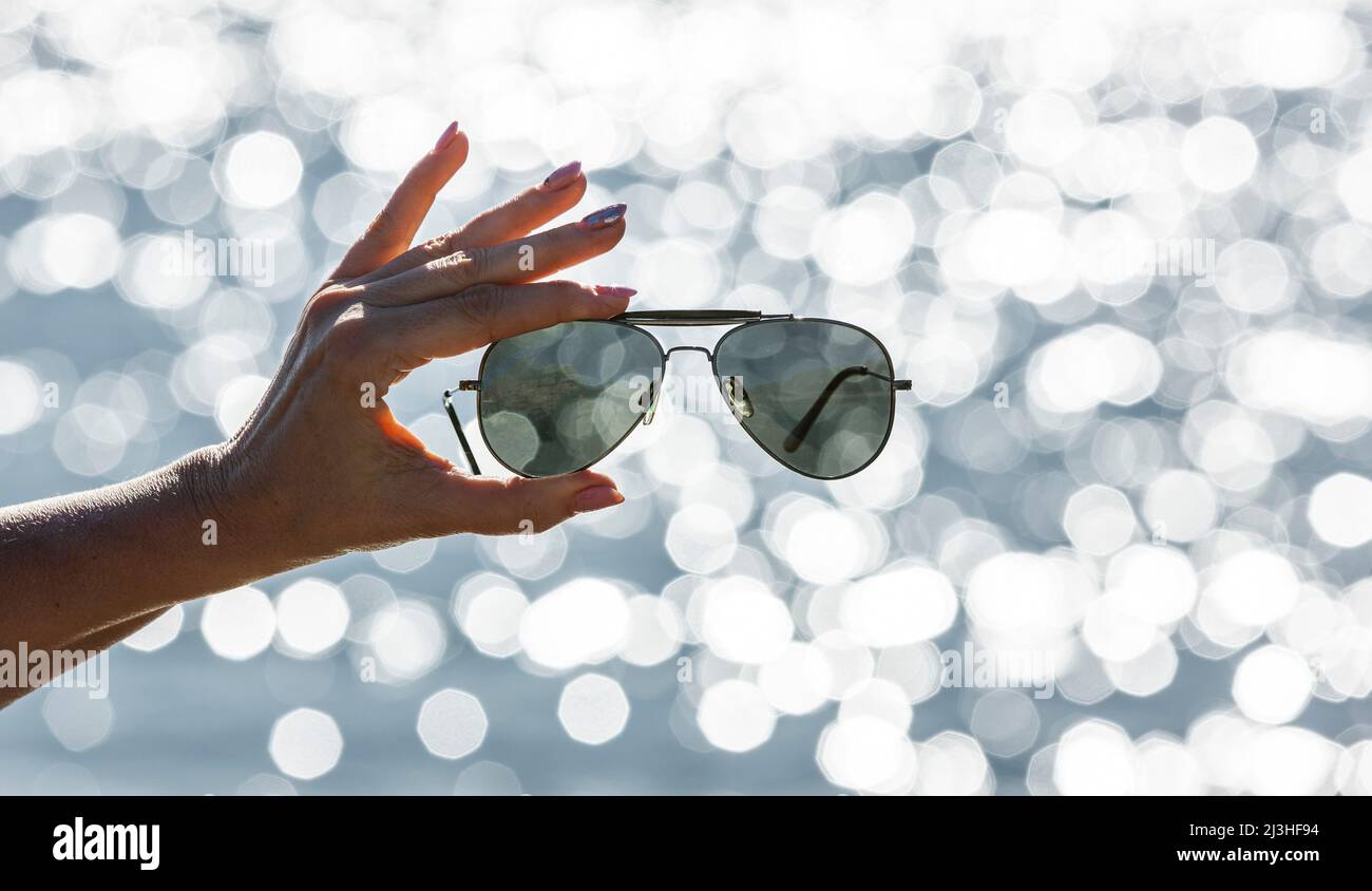 Sonnenbrille in einer Frauenhand vor verschwommenem Hintergrund mit Bokeh-Reflexen Stockfoto