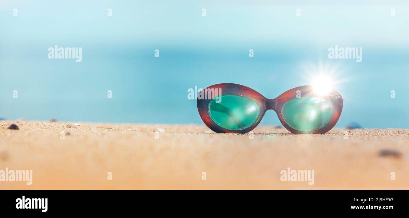 Vintage Sonnenbrille an einem Sandstrand mit blauem Meer im Hintergrund Stockfoto