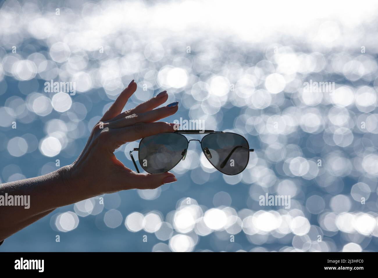Sonnenbrille in einer Frauenhand vor verschwommenem Hintergrund mit Bokeh-Reflexen Stockfoto
