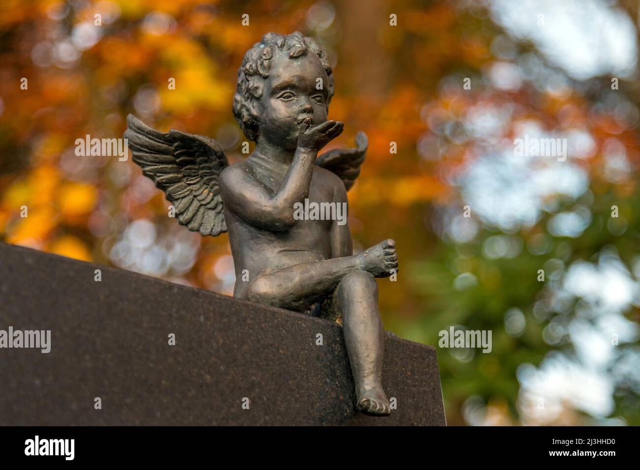 Ein Engel sitzt auf einem Grabstein und sendet einen Handkuss in den Himmel Stockfoto