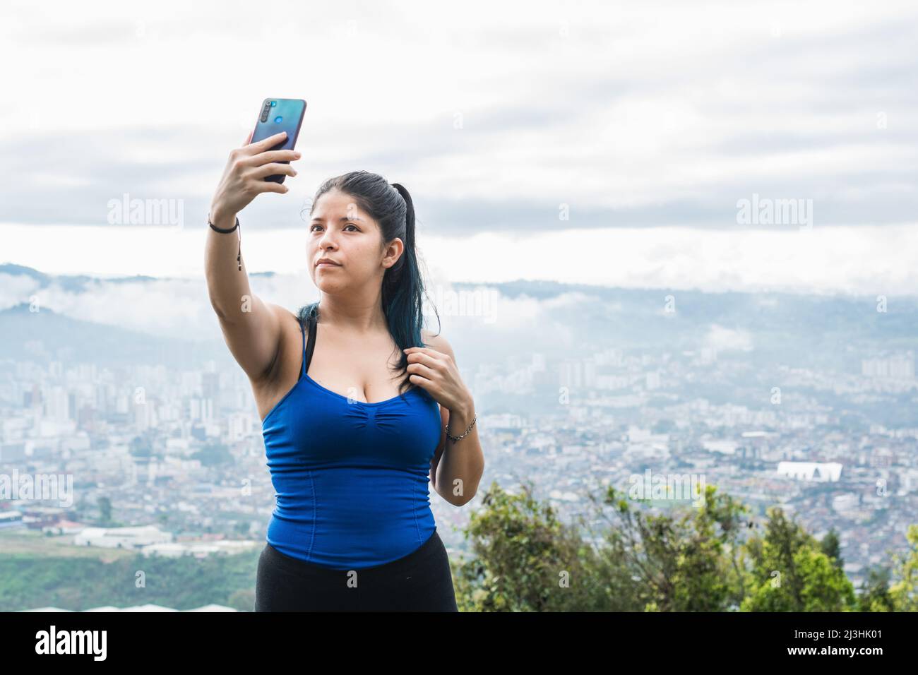 Mittellange Aufnahme einer jungen Frau. latin-Influencerin, die ein Selfie für ihre sozialen Netzwerke auf einem Berg macht, im Hintergrund die Stadt Pereira-Colom Stockfoto