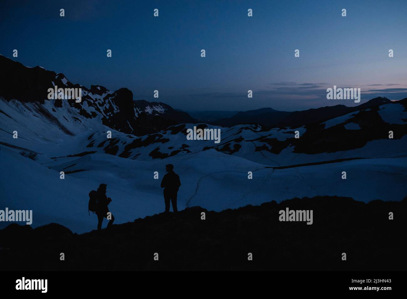Silhouette von zwei Menschen, die während des Sonnenaufgangs vor der Gletscherlandschaft stehen Stockfoto