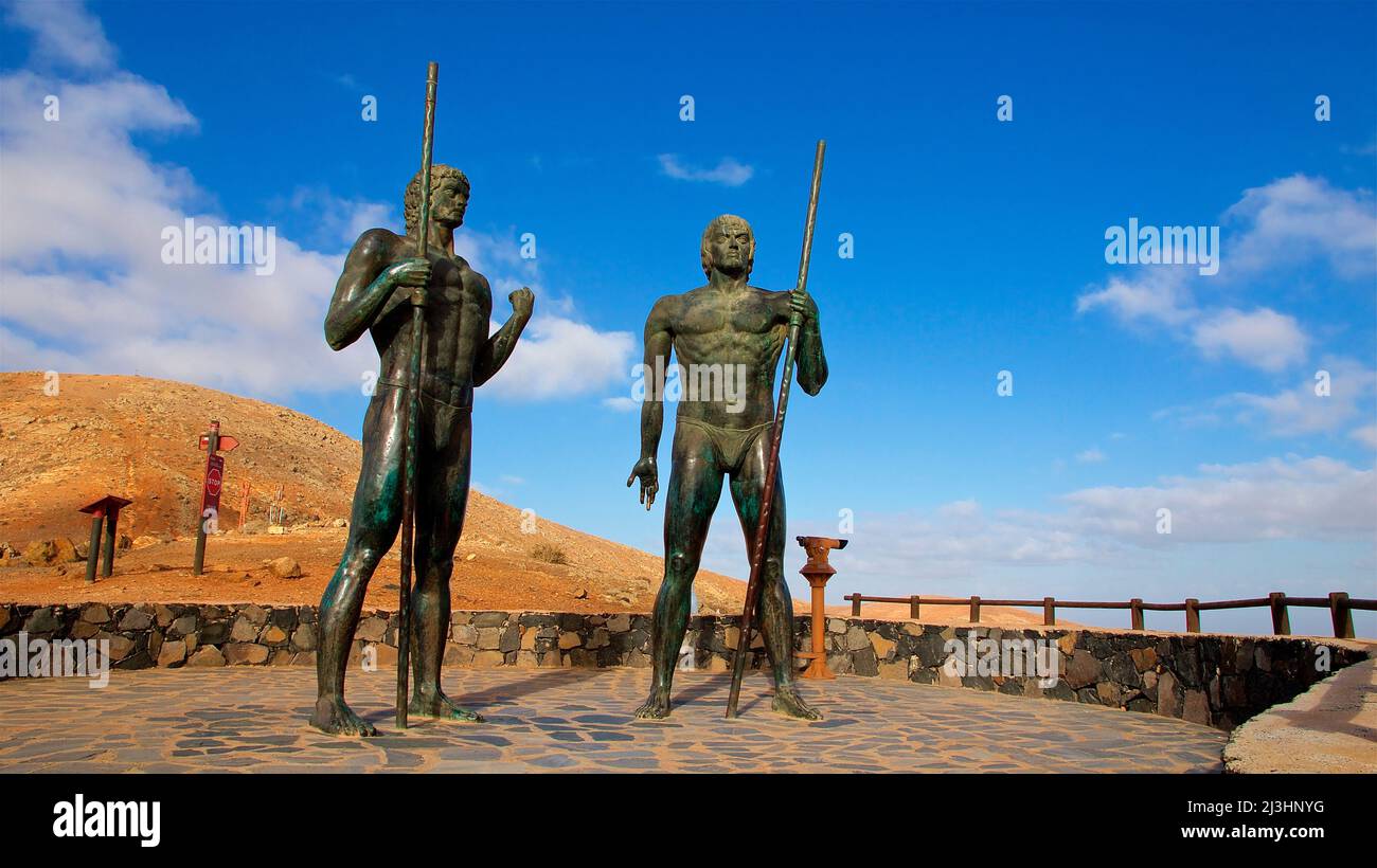 Spanien, Kanarische Inseln, Fuerteventura, Mirador Morro Velosa, Denkmal für die Guanchen. Zwei lebensgroße Bronzestatuen, bewaffnet mit Speeren, die die Krieger der Guanchen darstellen, blauer Himmel, weiße Wolken Stockfoto