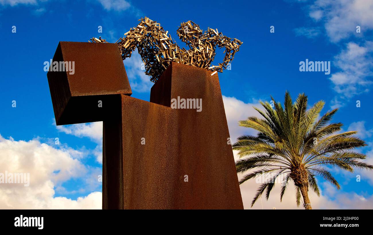 Spanien, Kanarische Inseln, Fuerteventura, Hauptstadt, Puerto del Rosario, Kunstinstallation, rostiger Eisenblock, darauf sitzende Figur aus Metallteilen, Palme daneben, himmelblau mit weißen Wolken Stockfoto