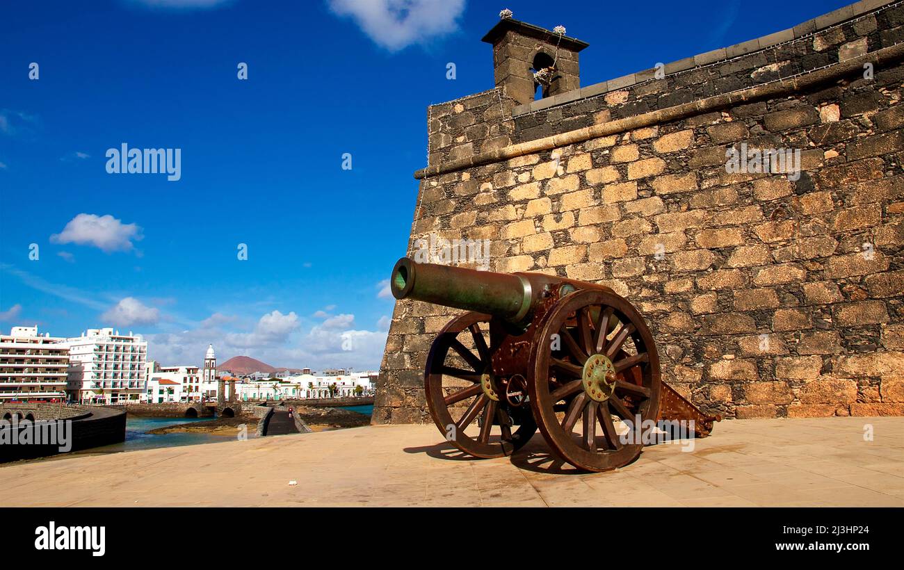 Kanarische Inseln, Lanzarote, Vulkaninsel, Hauptstadt Arrecife, Castillo de san Gabriel, mittelalterliche Kanone vor der Burg, im Hintergrund links Wolkenkratzer von Arrecife, himmelblau, einzelne weiße Wolken Stockfoto