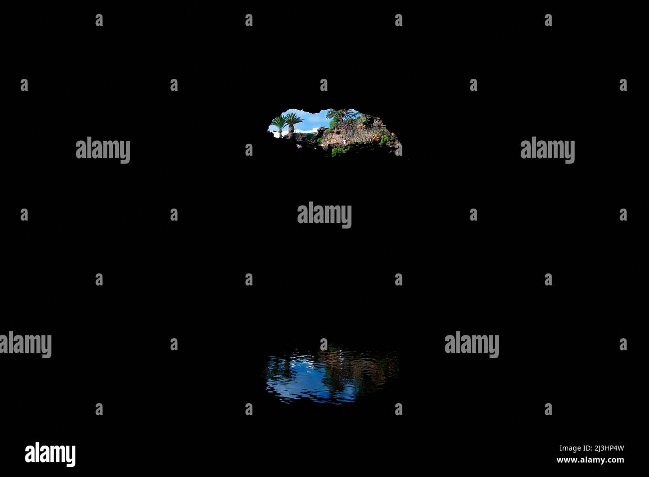 Kanarische Inseln, Lanzarote, Vulkaninsel, Jameos del Agua, entworfen von Cesar Manrique, einzigartiger vulkanischer Tunnel und Höhlen mit unterirdischem Konzertsaal, Restaurant und Salzsee, Blick vom Inneren der Höhle zurück zum Eingang, blauer Himmel, Palmen, Motiv reflektiert im glatten Wasser des Höhlensees Stockfoto