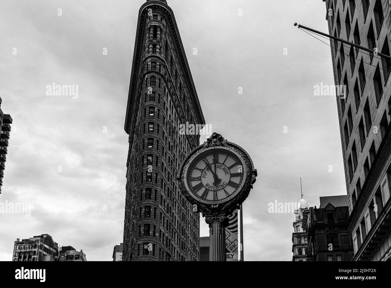 23 Street, New York City, NY, USA, Historic Flatiron or Fuller Building, ein 22-stöckiges, dreieckiges, stahlgerahmtes Wahrzeichen, das 1902 erbaut wurde und als einer der ersten Wolkenkratzer aller Zeiten und eine der berühmten New Yorker Straßenuhren gilt Stockfoto