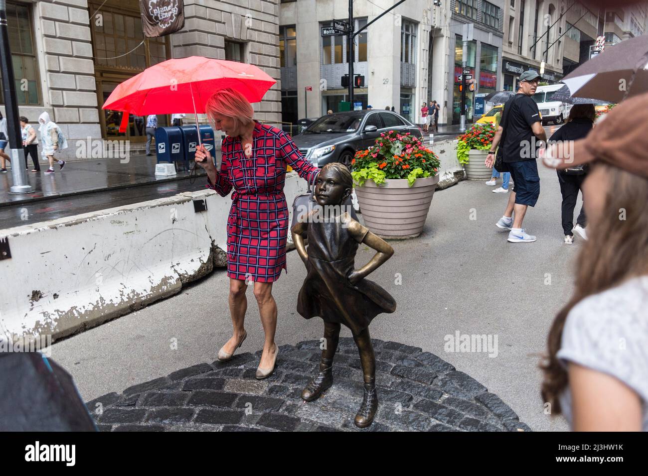 Financial District, New York City, NY, USA, Eine Dame mit einem Regenschirm, der neben der Statue „Fearless Girl“ von Kristen Visbal auf der Broad Street vor der New Yorker Börse steht Stockfoto