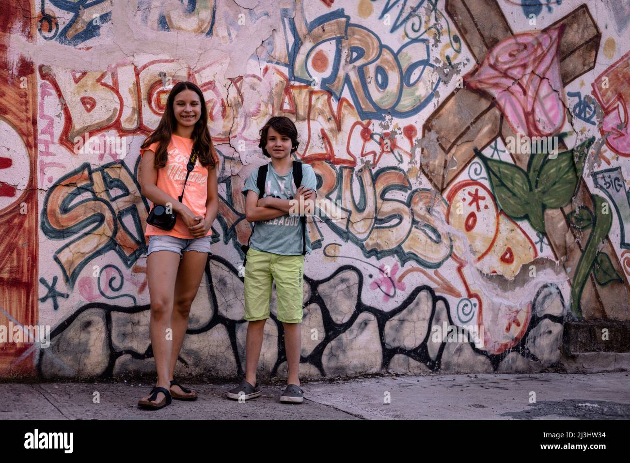 Lafayette Ave/Stuyvesant AV, New York City, NY, USA, 14 Jahre altes kaukasisches Teenager-Mädchen und 12 Jahre altes kaukasisches Teenager-Mädchen – beide mit braunen Haaren und sommerlichem Styling vor einem Graffiti in Brooklyn Stockfoto