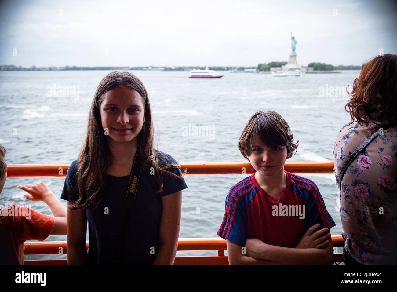 New York City, NY, USA, 14 Jahre altes kaukasisches Teenager-Mädchen und 12 Jahre altes kaukasisches Teenager-Mädchen – beide mit braunen Haaren und sommerlichem Styling auf der staten Island Ferry. Dahinter die Freiheitsstatue Stockfoto