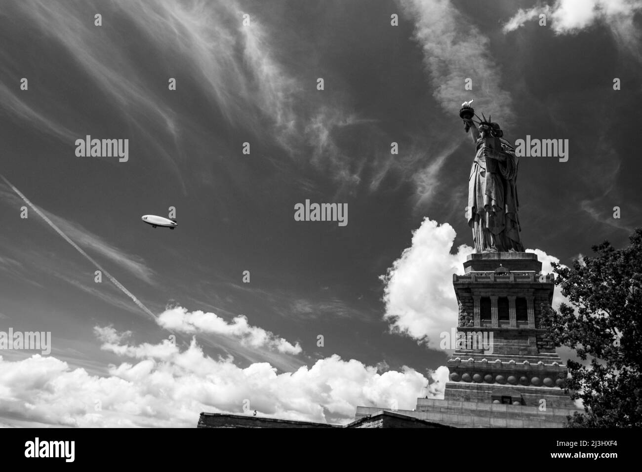 LIBERTY ISLAND, New York City, NY, USA, Freiheitsstatue vor blauem Himmel mit wunderschönem Wolkenhintergrund und einem Zeppelin Stockfoto