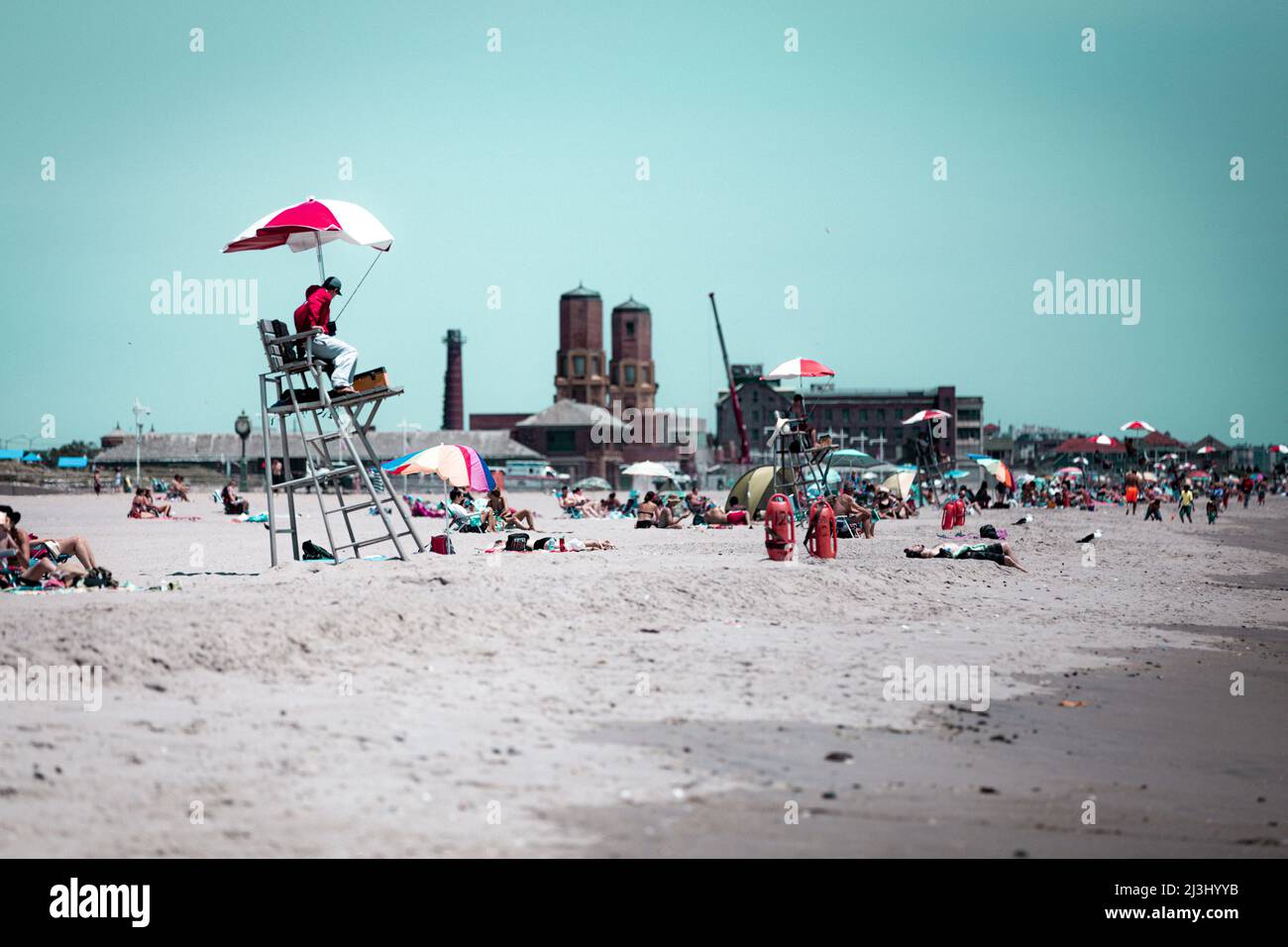 Breezy Point, New York City, NY, USA, Ein Rettungsschwimmer und viele Leute am Strand genießen einen schönen Tag und fragen sich, warum der Himmel so grün ist, im Hintergrund das Badehaus im JACOB RIIS PARK Stockfoto