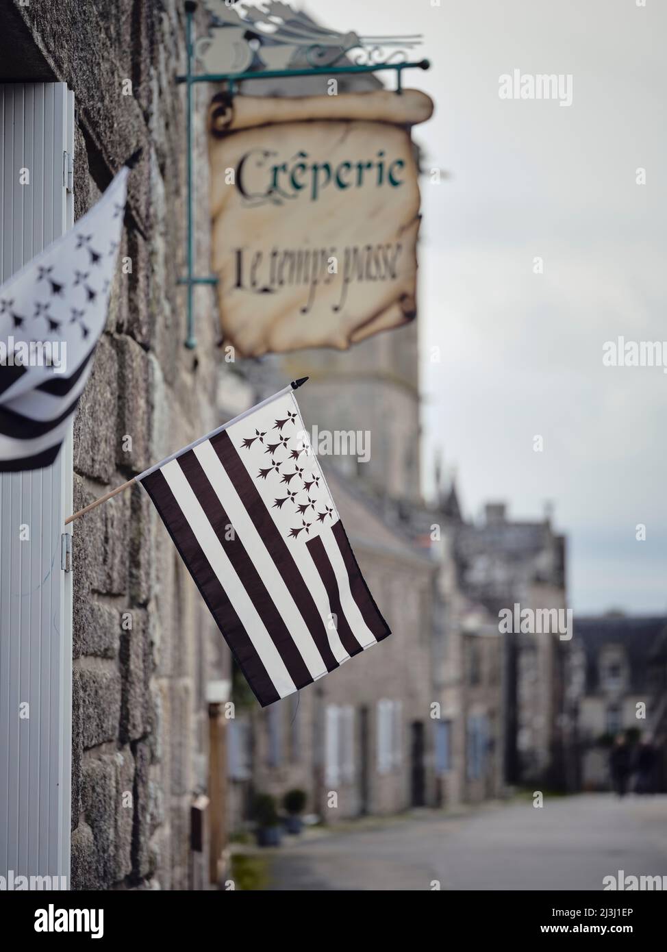 Die bretonische Flagge bei einem crêperie in Locronan im Departement Finistère in der Bretagne. Die Hütten wurden aus Granit gebaut und stammen aus dem 17.. Jahrhundert. Locronans historische Kulisse wurde in vielen Film- und Fernsehproduktionen gezeigt. Locronan ist ein beliebtes Ausflugsziel. Stockfoto