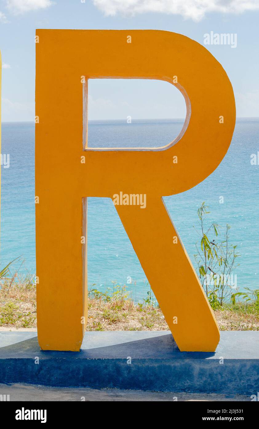 Orangene Betonskulptur eines Buchstaben R mit dem Karibischen Meer im Hintergrund. Stockfoto