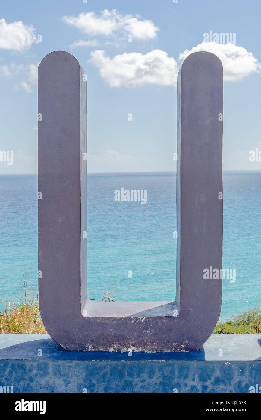 Violett bemalte Betonskulptur eines Buchstaben U mit dem Karibischen Meer im Hintergrund. Stockfoto