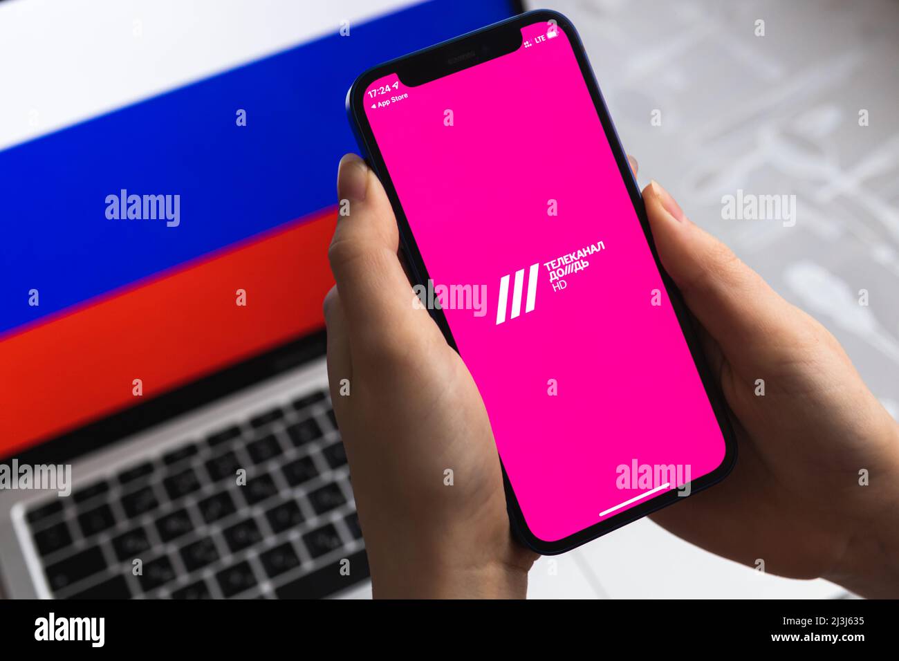 Poltava, Ukraine - 8. April 2022: Frau nutzt TV Rain App, Russland Flagge Hintergrund. Blockierte News-Anwendung in der Russischen Föderation, Handy mit ic Stockfoto