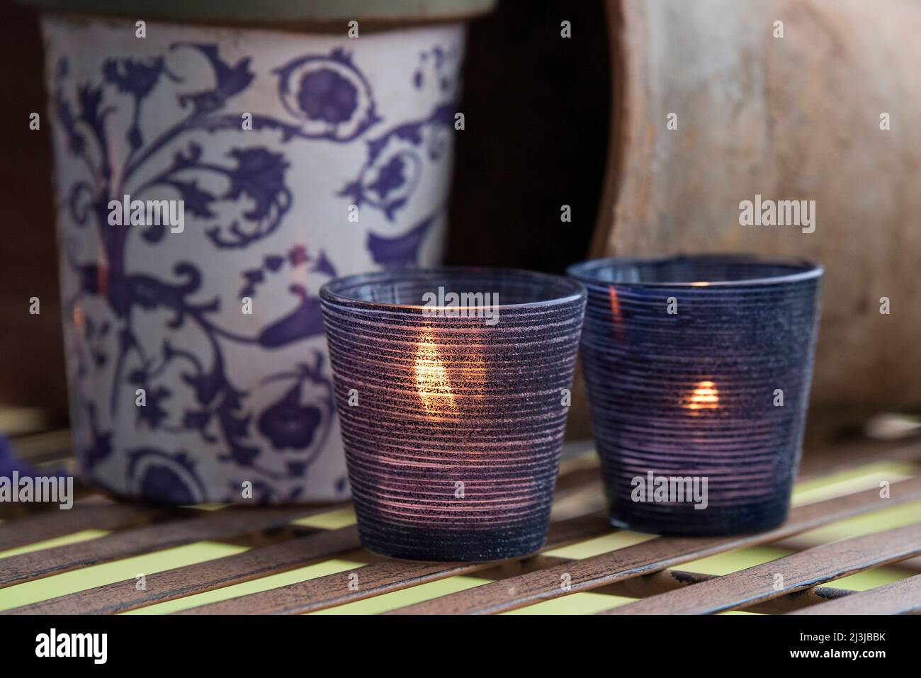 Stillleben, brennende Kerzen in Laternen zwischen Blumentöpfen, stimmungsvolle Dekoration in violetten und blauen Tönen Stockfoto