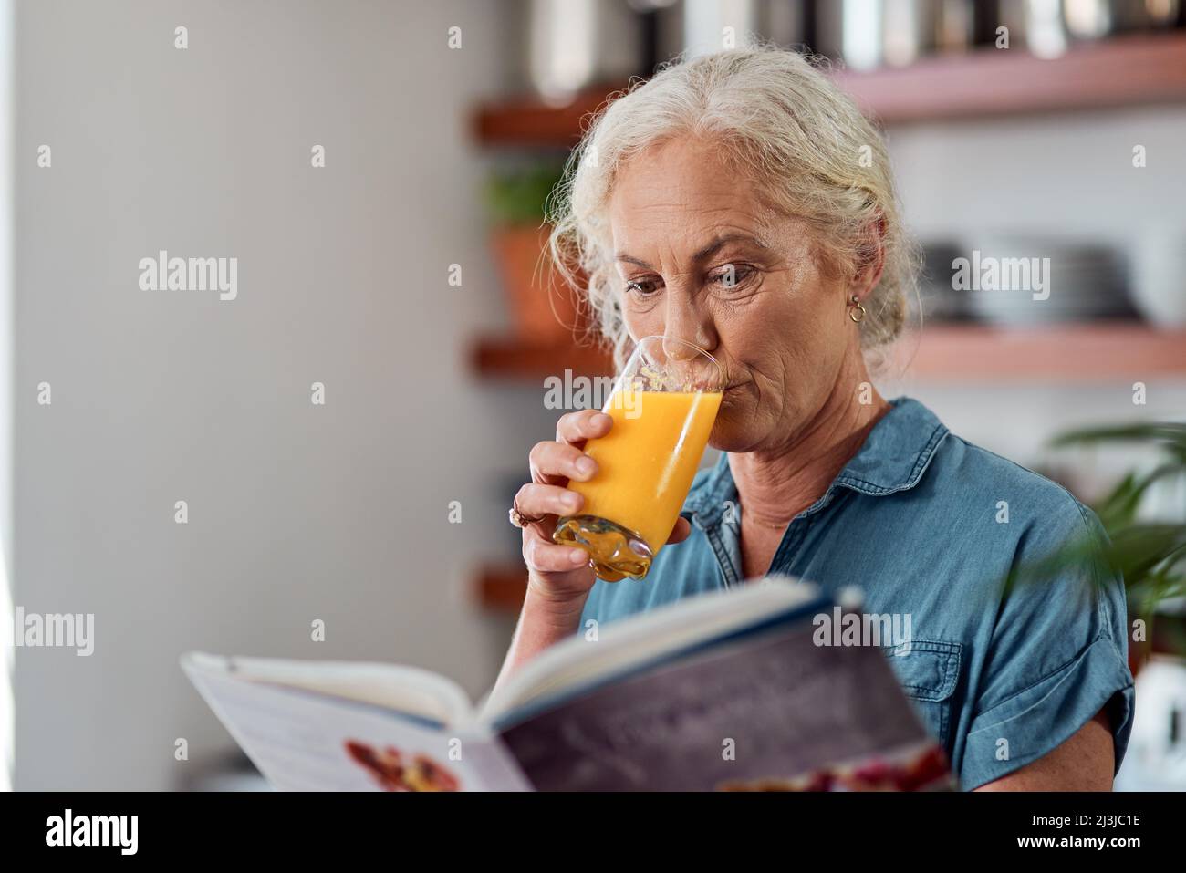 Es ist keine Diät, es ist eine Lebensweise. Aufnahme einer reifen Frau, die ein Buch liest, während sie zu Hause Orangensaft getrunken hat. Stockfoto
