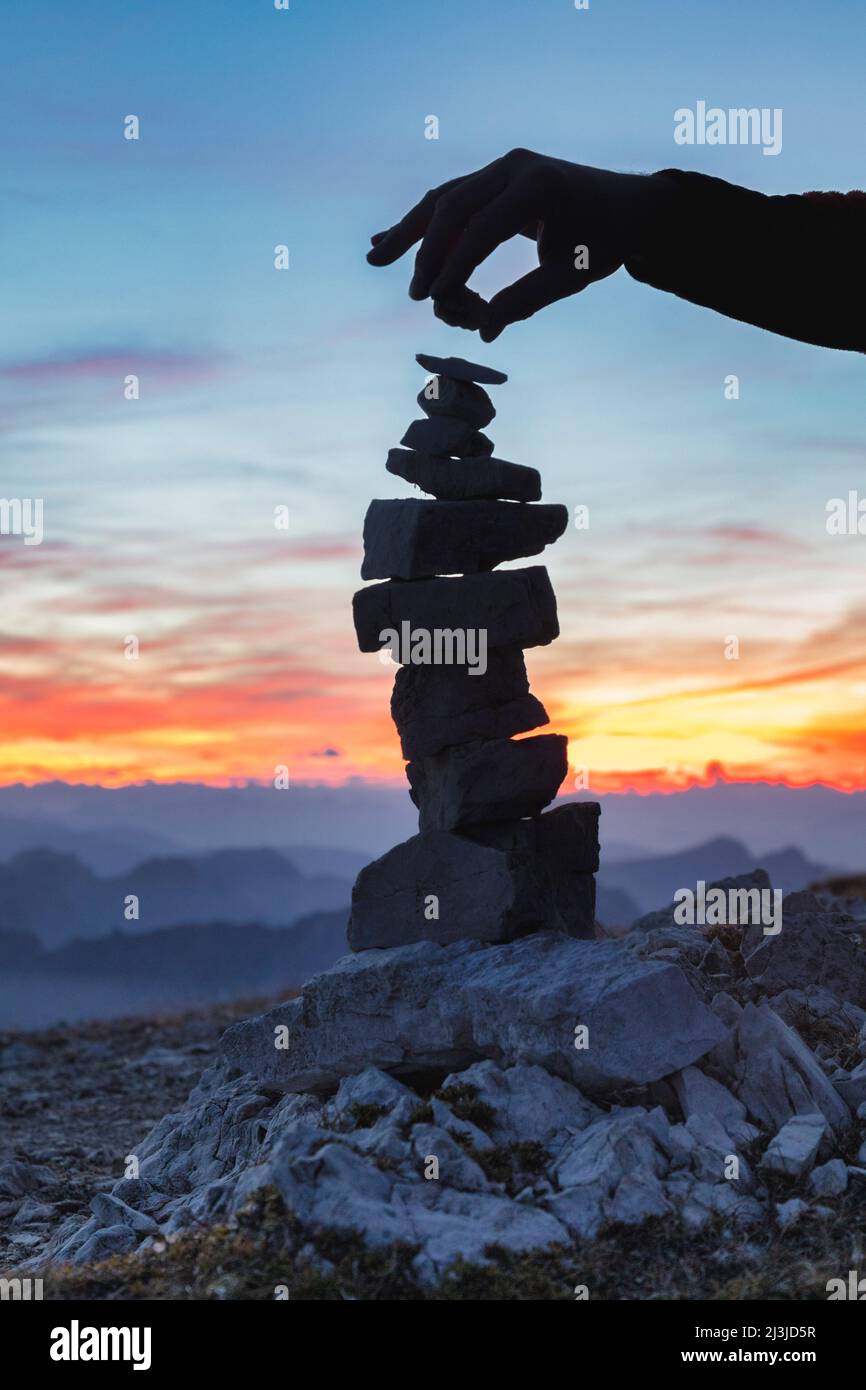 Europa, Italien, Südtirol - Südtirol, Arm und Hand in Silhouette fügt einem Steinmann / Cairn, Dolomiten, einen letzten Kieselstein hinzu Stockfoto