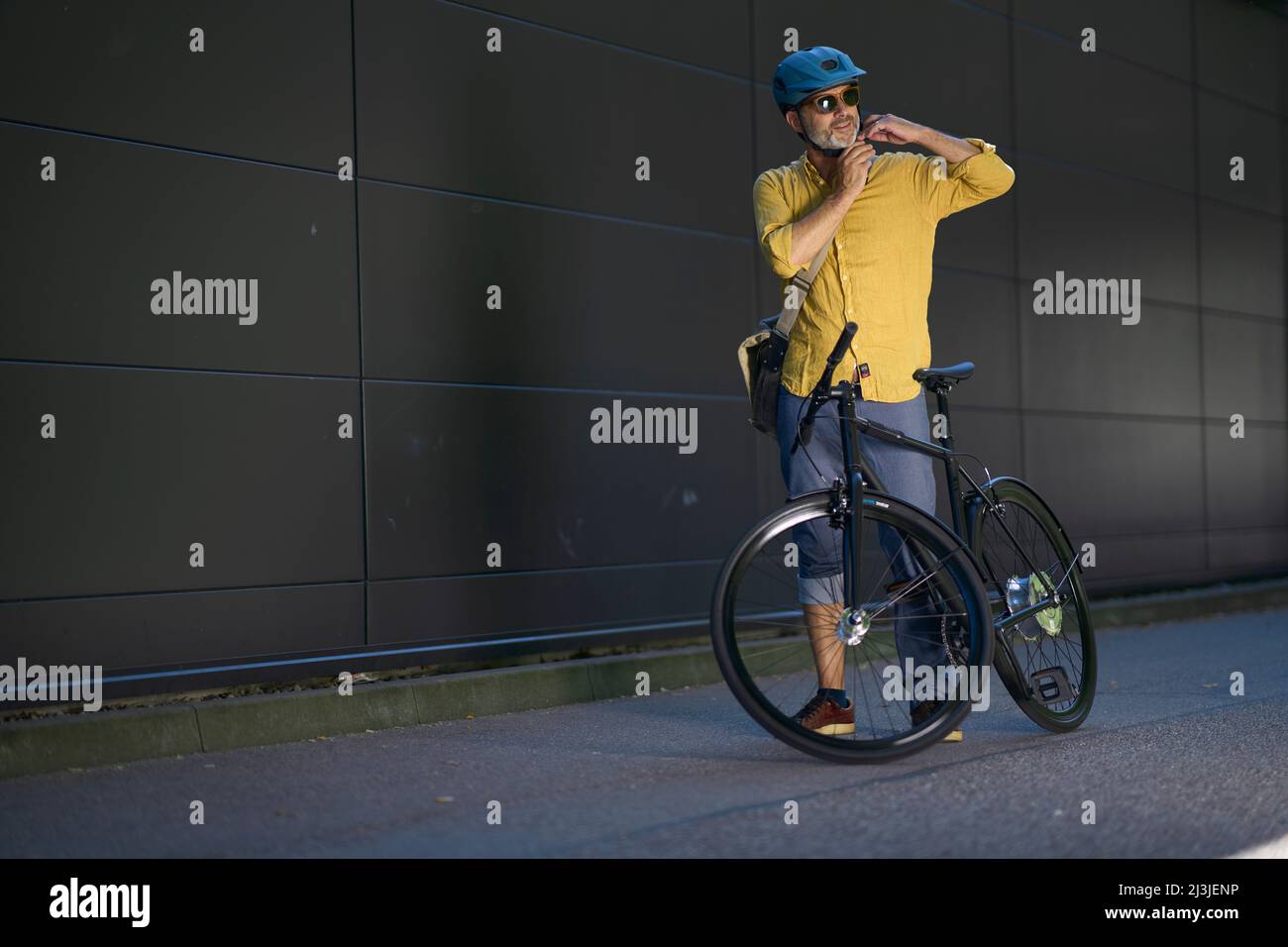 Mann mittleren Alters auf dem Fahrrad vor dunkler Fassade, urban, München, Deutschland Stockfoto