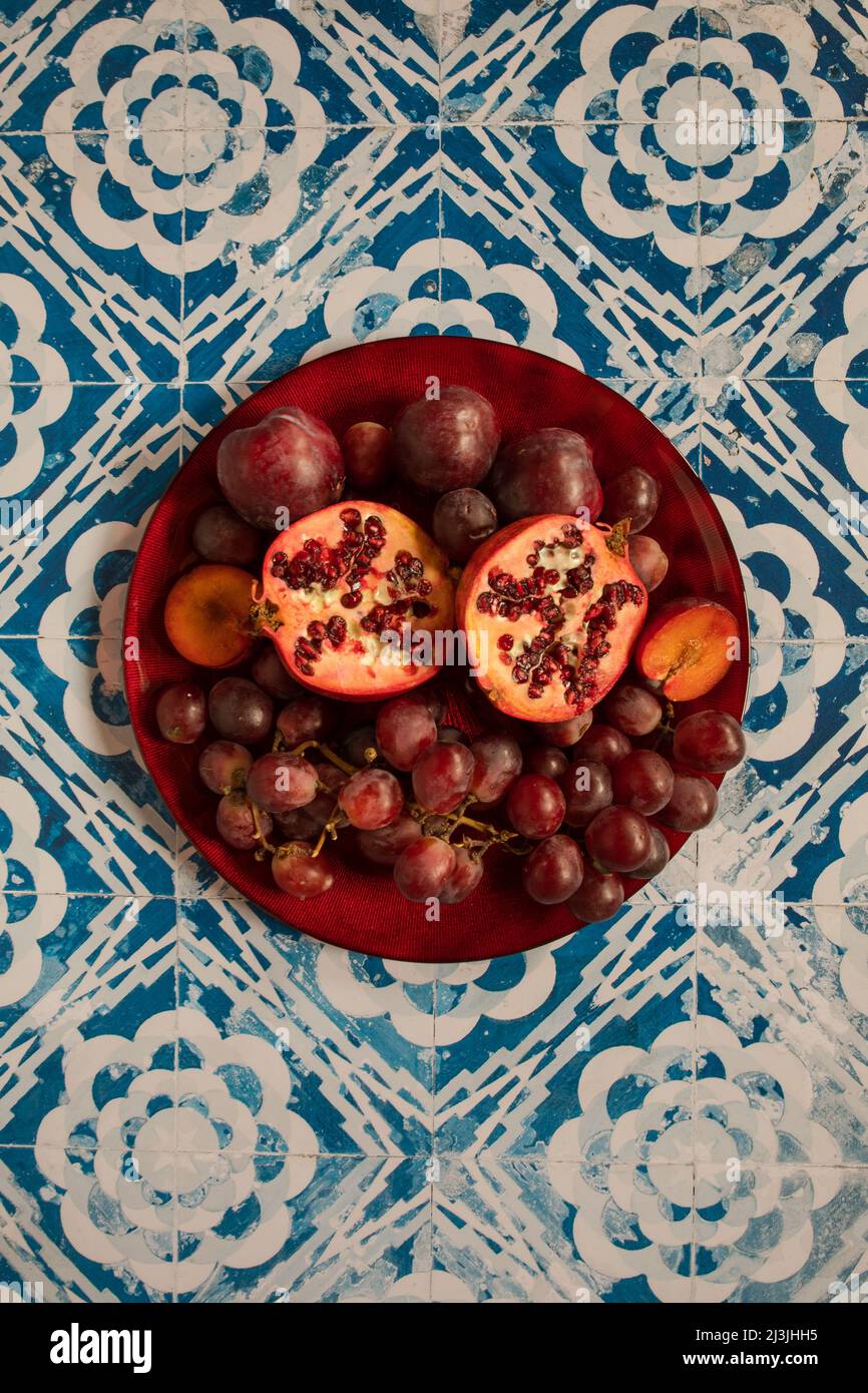 Stillleben rohe Pflaumen, Granatapfel und Trauben im Vintage-Hintergrund Stockfoto