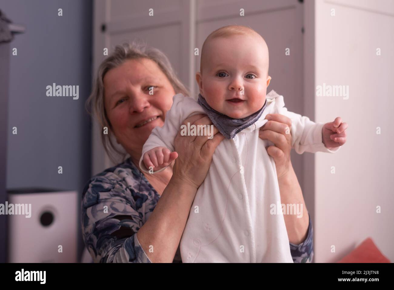 Ältere Großmutter, die zu Hause ein 7 Monate altes Baby in den Armen hält Stockfoto