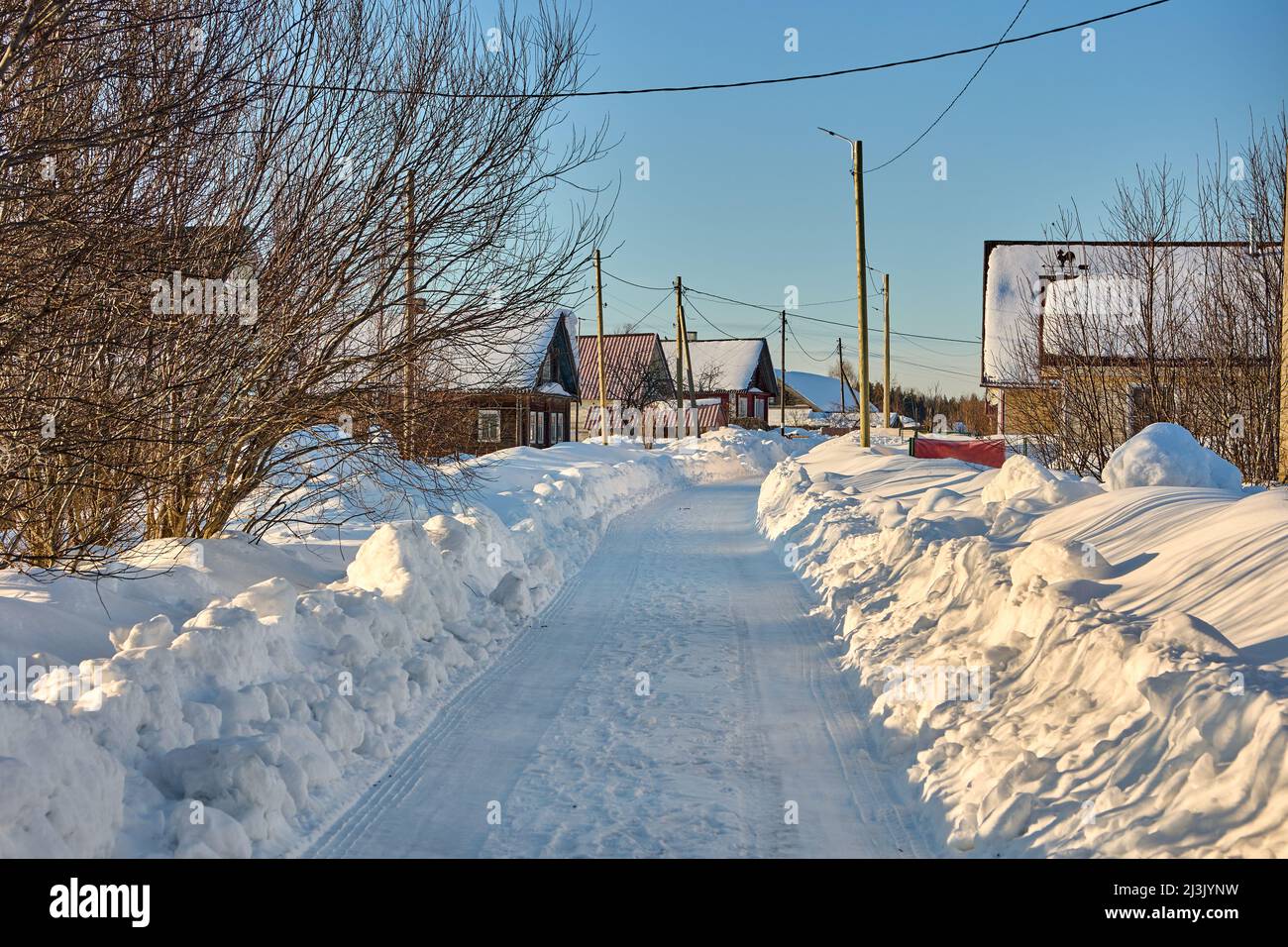 Verschneite Straße auf dem Land mit Schneeverwehungen in der Nähe im Winter. Stockfoto