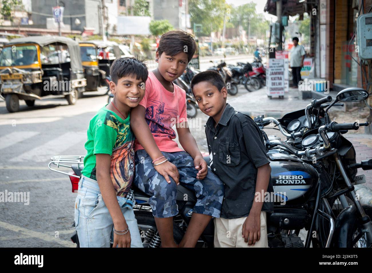 Drei Jungs versammeln sich auf einer Straße um ein Motorrad und schauen in die Kamera; Amritsar, Punjab, Indien Stockfoto