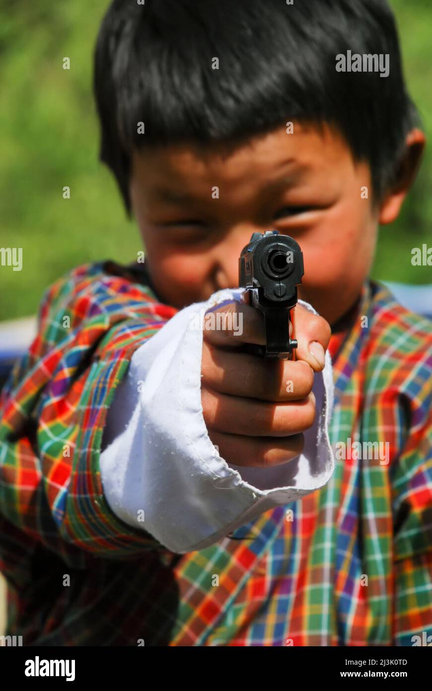 Ein Junge in traditioneller Kleidung richtet eine Spielzeugpistole auf die Kamera; Paro, Bhutan Stockfoto