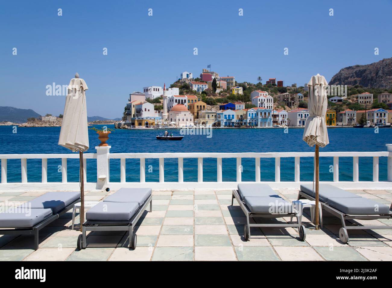 Liegestühle und Sonnenschirme auf einer Hotelterrasse mit Blick auf den Hafen und farbenfrohe Gebäude entlang der Küste über den Hafen Stockfoto