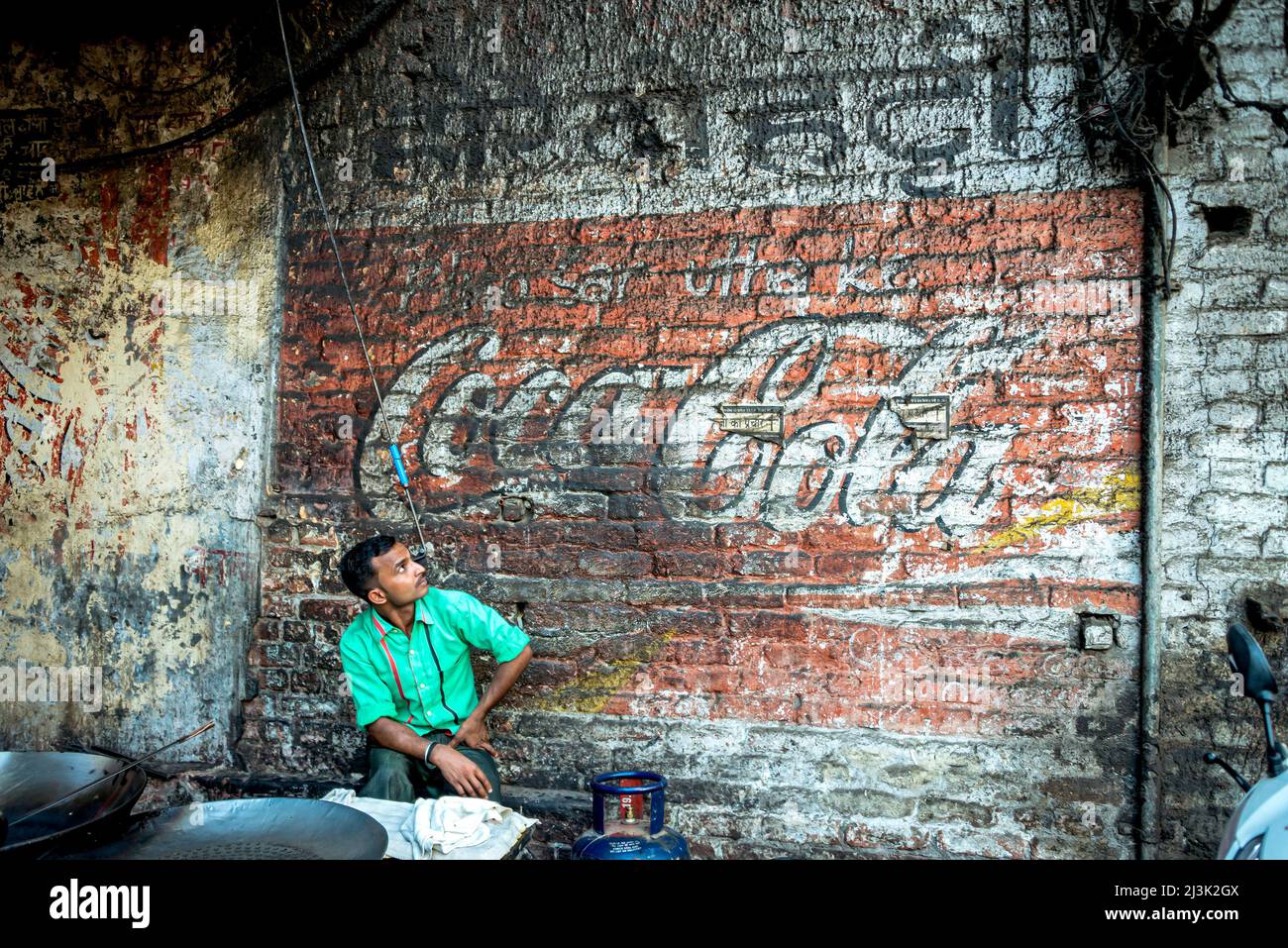 Der Mensch sitzt und schaut auf ein verblasstes Cola-Schild, das auf einer Ziegelmauer gemalt ist; Amritsar, Punjab, Indien Stockfoto