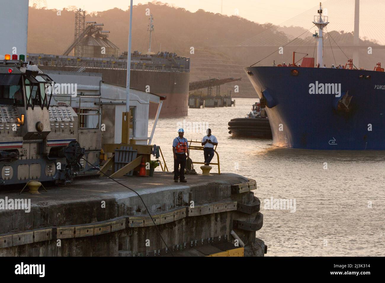 Bei Pedro Miguel Locks, in der Nähe der Centennial Bridge, stehen und arbeiten mehrere Männer neben dem Panamakanal, Ausrüstung und großen Schiffen in Panama Stockfoto