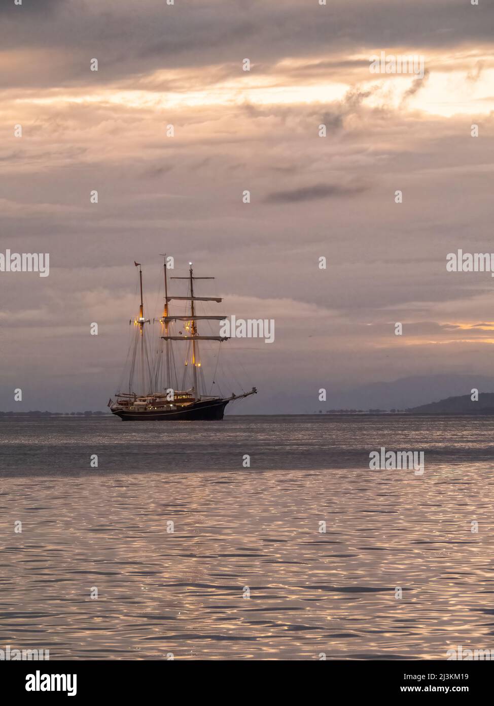 Hohes Segelschiff in tropischer Bucht im Morgengrauen, mit weichen, warmen Farben. Stockfoto