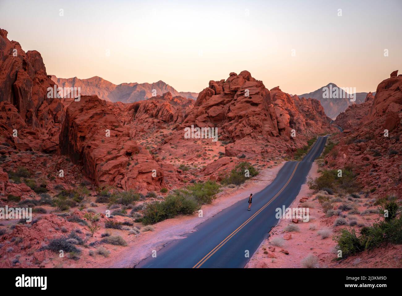 Eine Frau fährt im Valley of Fire State Park auf einer leeren Wüstenstraße auf Skateboards. Stockfoto