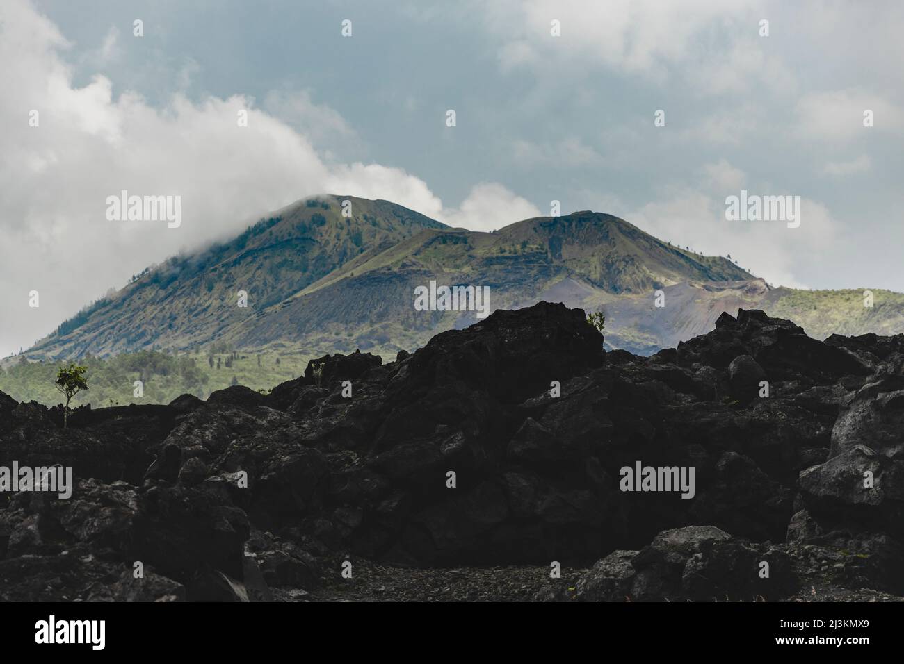 Vulkanisches Gestein und Blick auf den Berg Batur (Kintamani Volcano) in Süd-Batur mit bewölktem Himmel; Kintamani, Bangli Regency, Bali, Indonesien Stockfoto