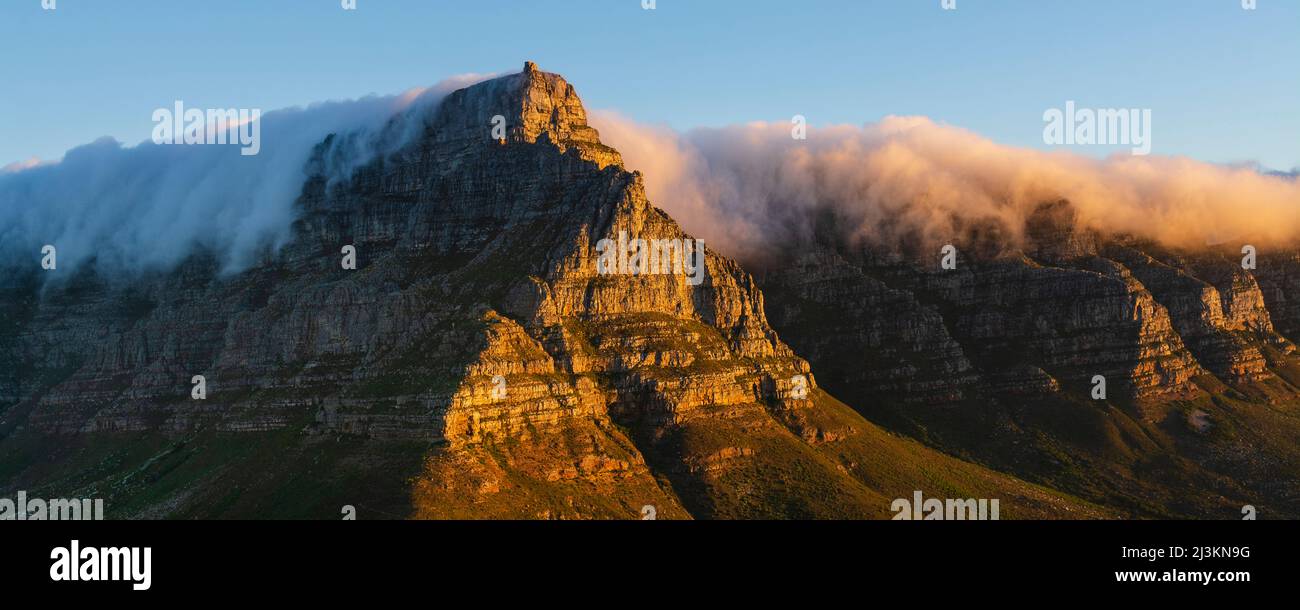 Ein Blick auf den sonnenbeschienenen Tafelberg von Lion's Head mit einer Wolkenformation, die einen Tischlappen-Effekt über den Berggipfeln erzeugt Stockfoto