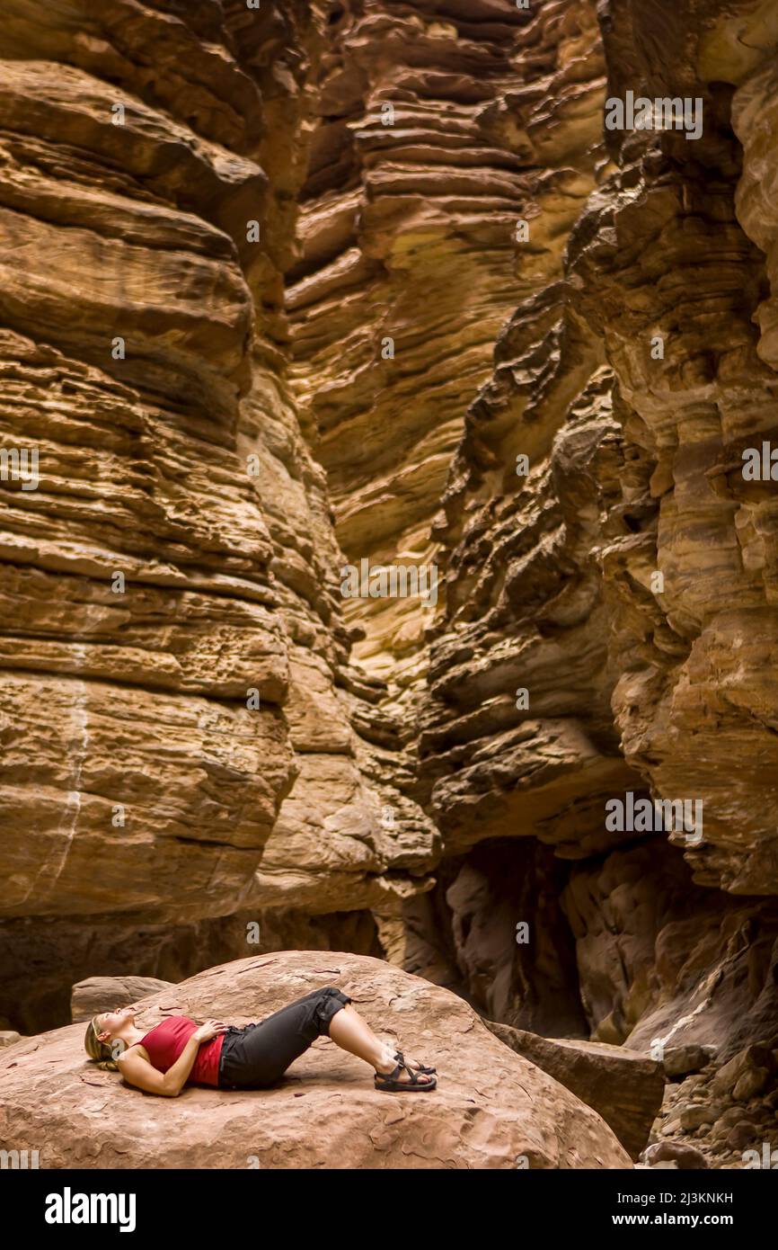 Ein Wanderer, der sich auf einem großen Felsen im Blacktail Canyon an der Colorado River Mile 120 beim Arizona Highways Photography Workshop entspannt Stockfoto
