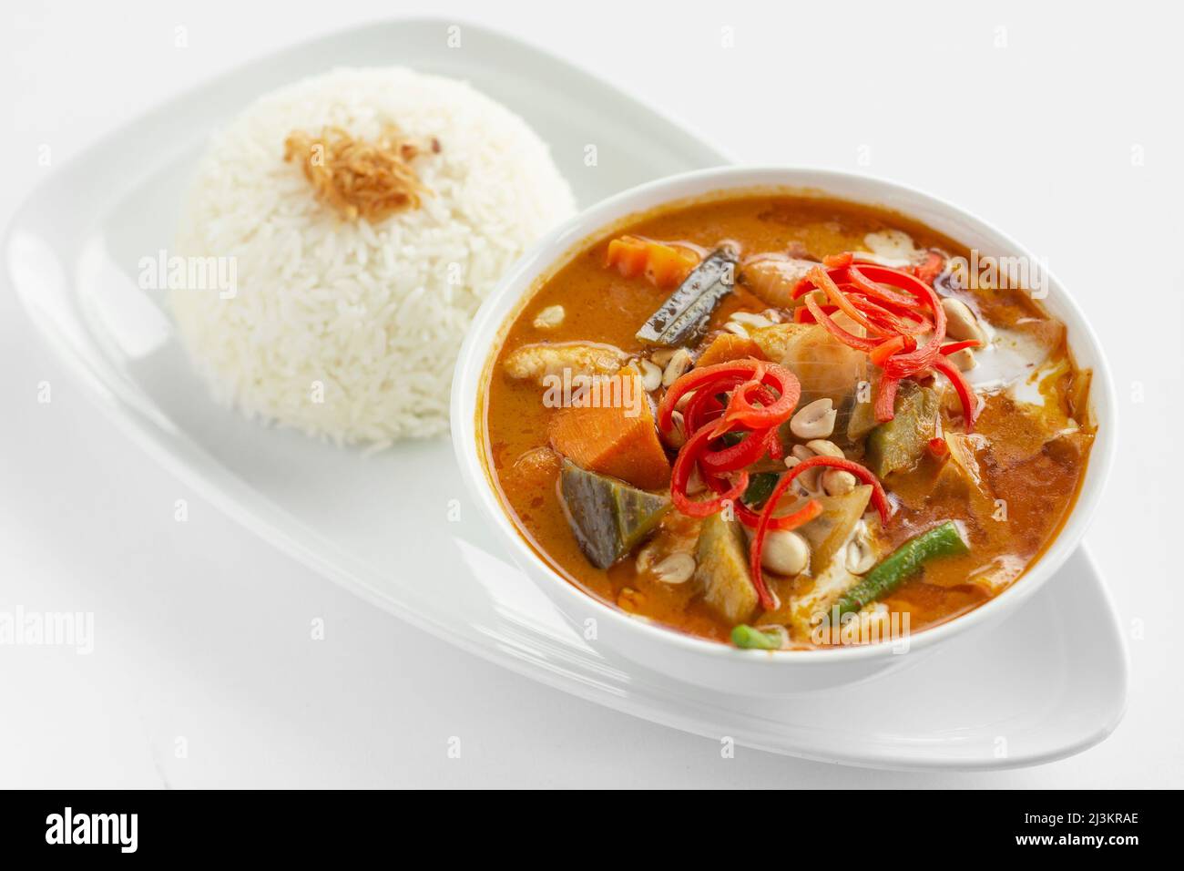 Traditionelles würziges thailändisches Huhn mit rotem, gedämpftem Reis auf weißem Hintergrund Stockfoto