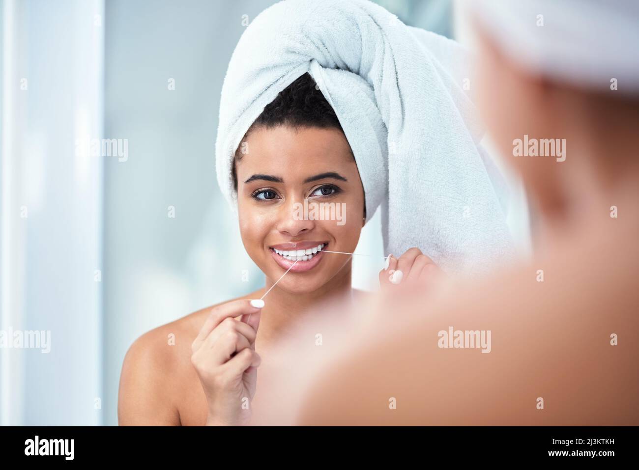 Zahnseide für ein sauberes Lächeln. Aufnahme einer Frau, die ihre Zähne mit einem Handtuch um ihren Kopf gewickelt hat. Stockfoto