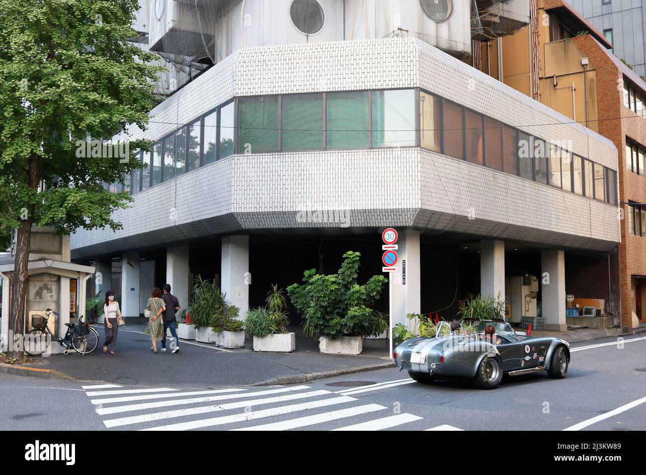 TOKIO, JAPAN - 10. Oktober 2021: Blick auf die Straße mit einem klassischen Sportwagen, der am Nakagin Capsule Tower in Tokio vorbeifährt. Etwas Bewegungsunschärfe. Stockfoto