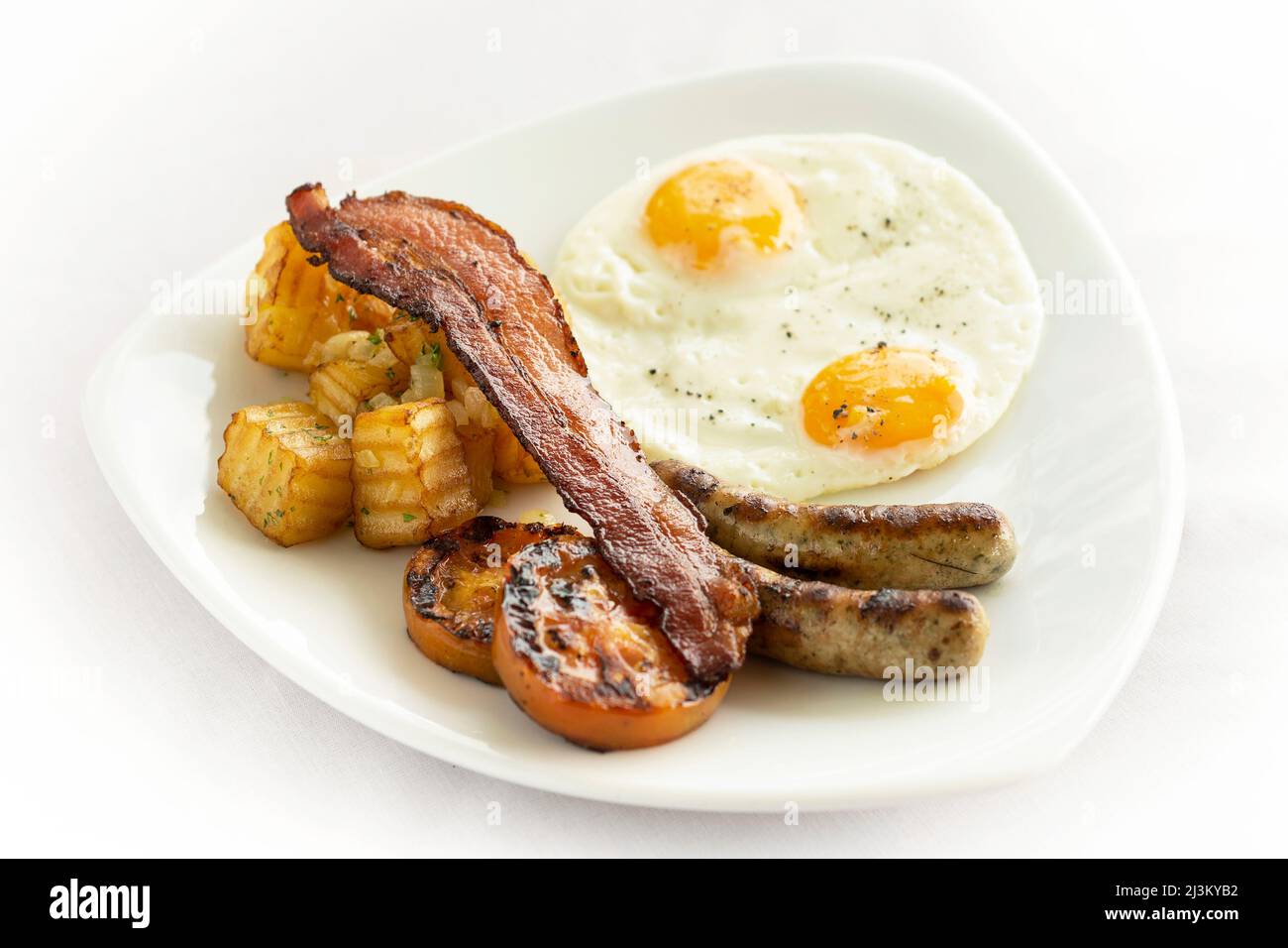 australisches Frühstück mit Spiegeleiern, Wurst, Speck und Kartoffeln auf weißem Hintergrund Stockfoto