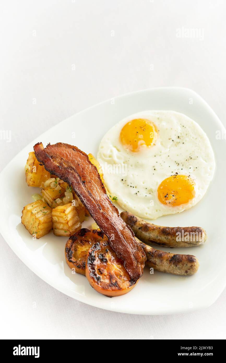 australisches Frühstück mit Spiegeleiern, Wurst, Speck und Kartoffeln auf weißem Hintergrund Stockfoto