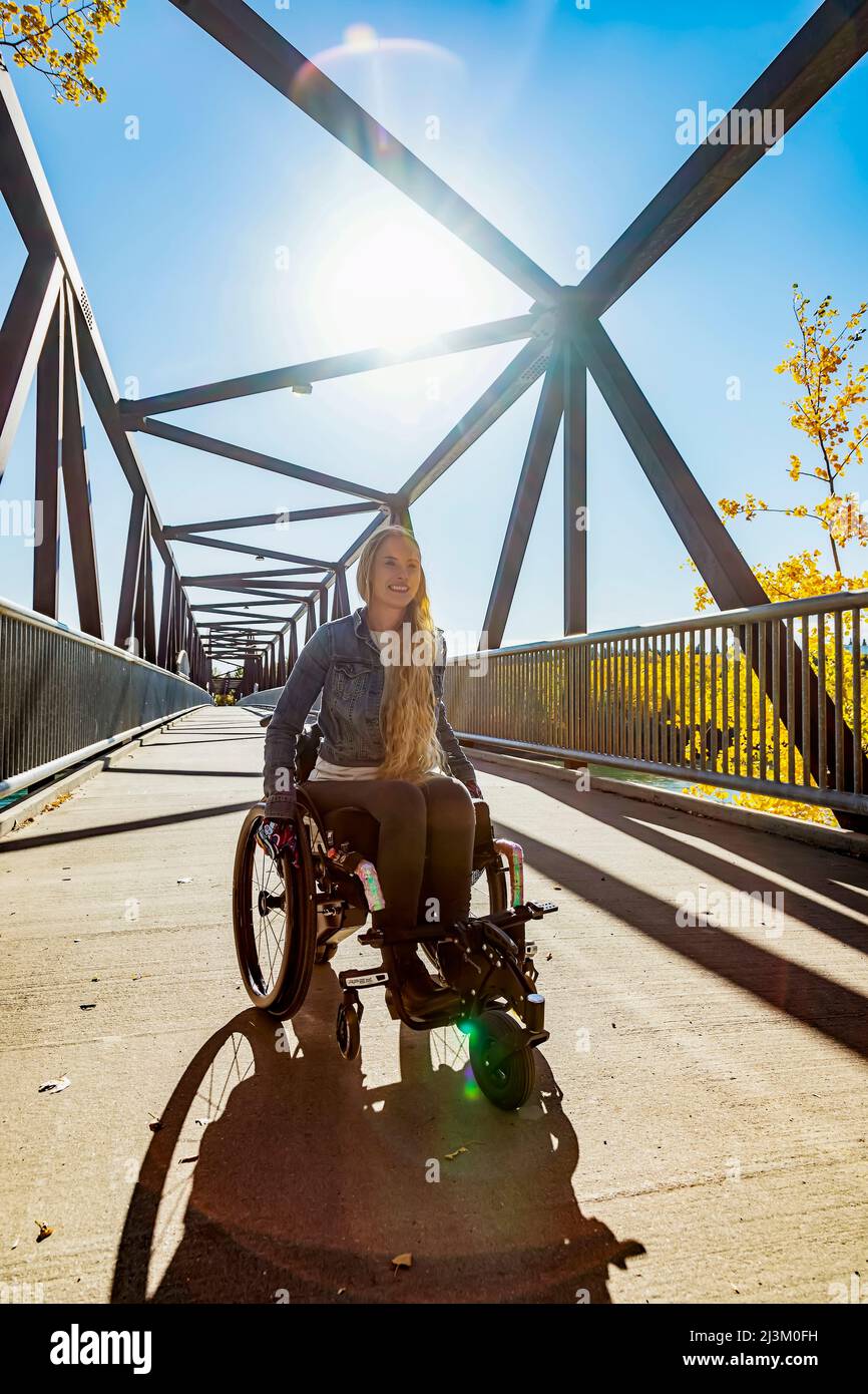 Eine junge querschnittsgelähmte Frau, die an einem schönen Herbsttag mit ihrem Rollstuhl über eine Brücke geht; Edmonton, Alberta, Kanada Stockfoto