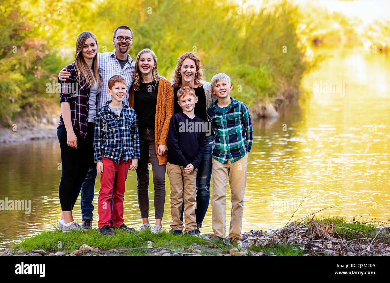 Siebenköpfige Familie, die im Herbst in einem Stadtpark am Wasser für ein Familienportrait steht; Edmonton, Alberta, Kanada Stockfoto
