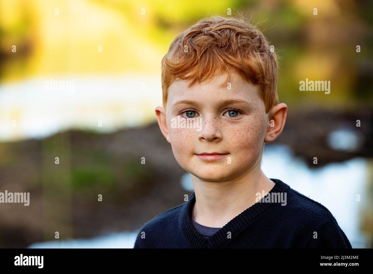 Outdoor-Porträt eines Jungen mit roten Haaren und Sommersprossen und verschwommenen Herbstfarben im Hintergrund; Edmonton, Alberta, Kanada Stockfoto