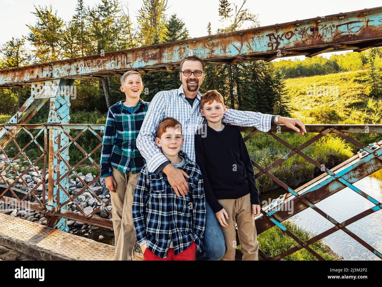 Außenportrait eines Vaters mit drei Söhnen, die auf einer Brücke in einem Park stehen; Edmonton, Alberta, Kanada Stockfoto